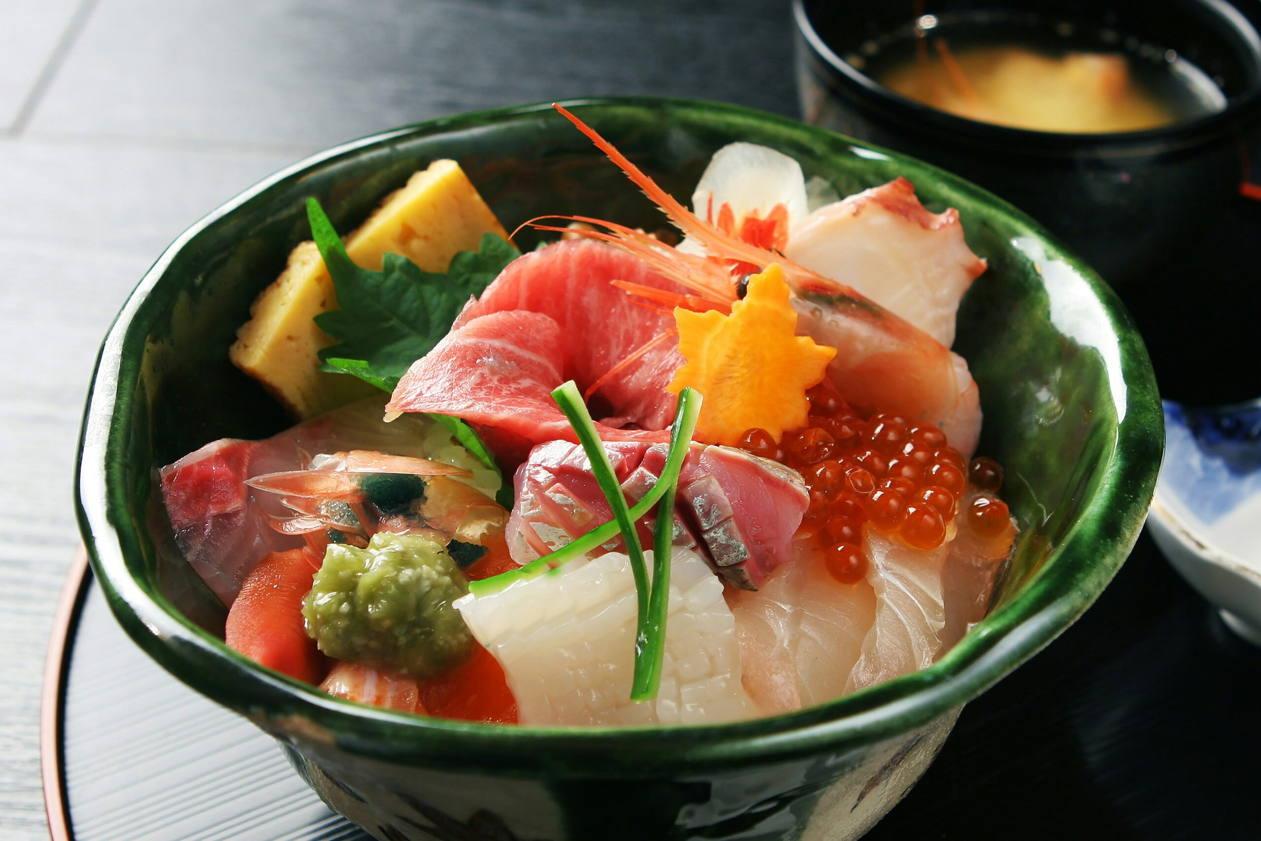 A bowl of sashimi and a cup of soup on a table