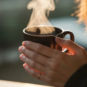 A close-up, cinematic shot of a person's hands gently closing a sleek laptop on a wooden desk. Next to the laptop is a small, lit ceramic candle and a steaming mug of tea, symbolizing the mindful transition from work to rest. Soft, warm late afternoon lighting, highly detailed, photorealistic.