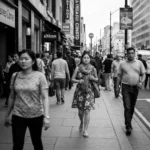 A serene, minimalist illustration of a person sitting peacefully on a grassy hill, looking up at a vast, clear blue sky where small, distinct clouds are passing by. The clouds contain faint, abstract shapes representing thoughts. The lighting is soft and warm, conveying a sense of emotional distance and calm awareness.