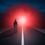 A lone figure standing at the edge of a perfectly paved, brightly lit road that abruptly transitions into a thick, mysterious, glowing mist. Cinematic lighting, conceptual photography, high contrast between the safe path and the unknown.