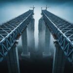 A highly detailed, cinematic shot of a massive, unfinished bridge over a foggy chasm. The bridge is 90% complete, but a sheer, daunting gap remains before the other side. High contrast, architectural photography, moody lighting, symbolizing the 'Last Mile Penalty'.