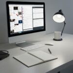 A minimalist workspace with a computer screen showing a chaotic, overflowing inbox and social media feeds, contrasting with a calm, blank notebook on a clean wooden desk. Cinematic lighting, photorealistic, high contrast.