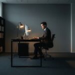 A minimalist, well-lit home office featuring a wooden standing desk. A person is captured mid-stretch, reaching their arms upward, with soft natural light streaming through a large window, highlighting the dust motes in the air. High-resolution, cinematic lighting, architectural photography style.