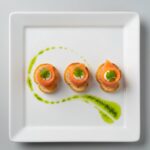 A top-down view of a stark white rectangular porcelain plate featuring three perfectly identical canapés. Each canapé consists of a crisp crostini, a delicate fold of smoked salmon, a tiny dollop of crème fraîche, and a single micro-cilantro leaf. The plate has a vibrant green herb oil swoosh across the negative space. High-end culinary photography, bright natural lighting.